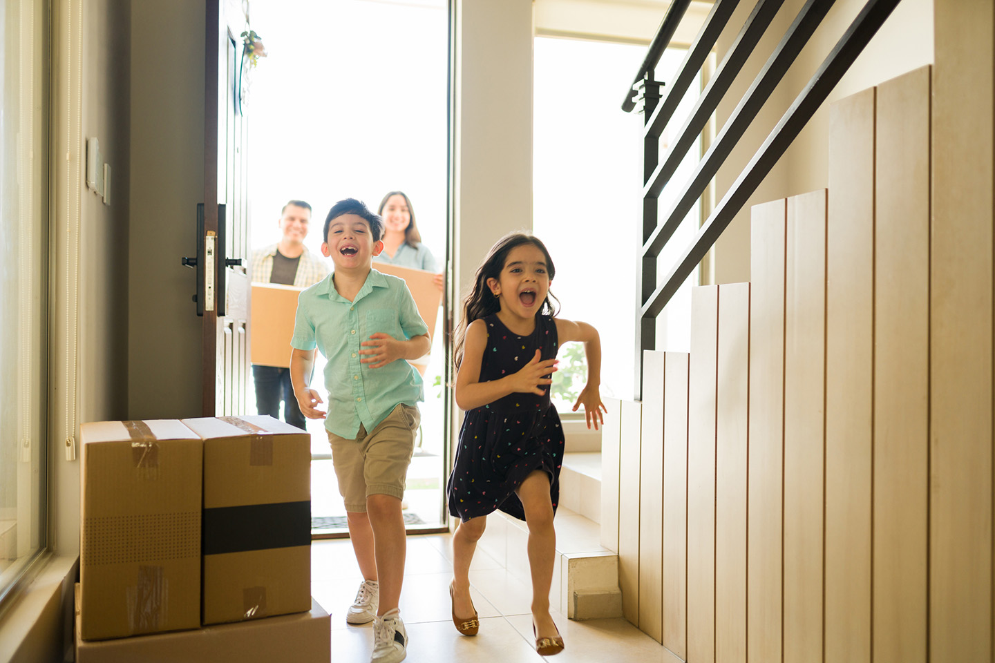 Parents and two kids run into their new home carrying moving boxes