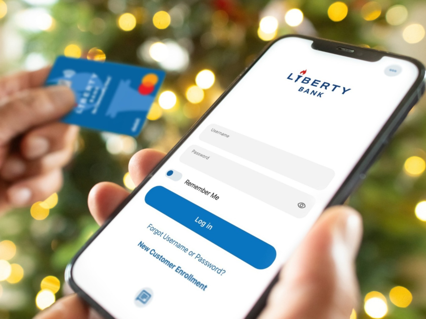 close up of person on mobile banking app with liberty bank card in hand and holiday decor in the background