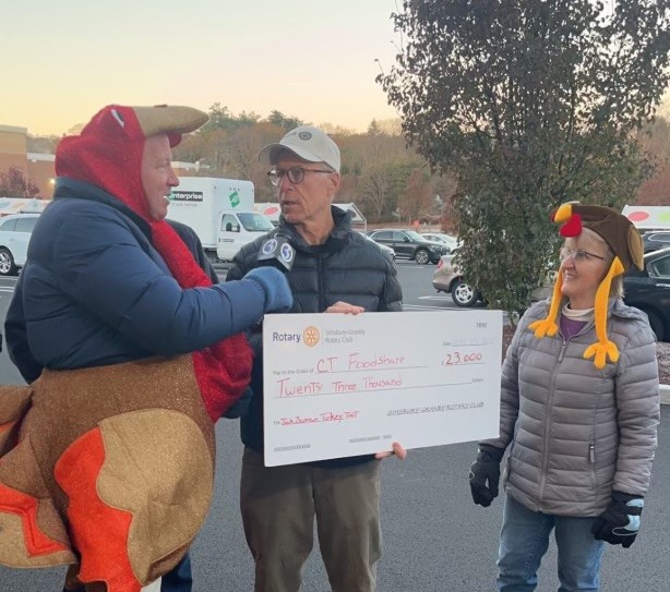 A newscaster, dressed in a turkey costume, interviews two Rotary Club leaders